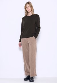 Dunkelgrüner langärmeliger Pullover mit Rundhalsausschnitt, kombiniert mit beigen, strukturierten, weit geschnittenen Hosen und schwarzen Stiefeletten.