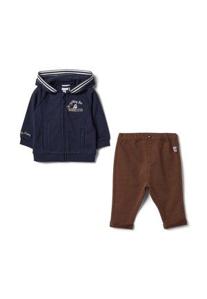 Marineblauwe capuchonjas met rits en tekstdetail, gecombineerd met bruine broek met elastische taille, beide gemaakt voor peuters.