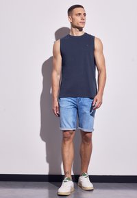 Marinblå ärmlös skjorta, ljusblå denimshorts med upprullade slut, och vita sneakers med gröna detaljer. Enkelt mönster, avslappnad passform.