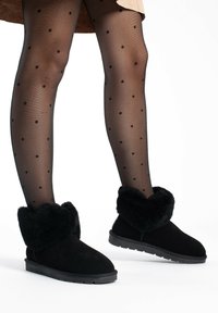 Botas negras hasta el tobillo con un suave puño de piel, confeccionadas en ante, con suela de goma plana y diseño de puntera redondeada.