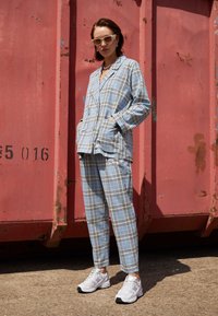 Ljusblått rutigt pyjamas-set med en knäppjacka och matchande byxor. Vita sneakers med svarta accenter kompletterar outfiten.