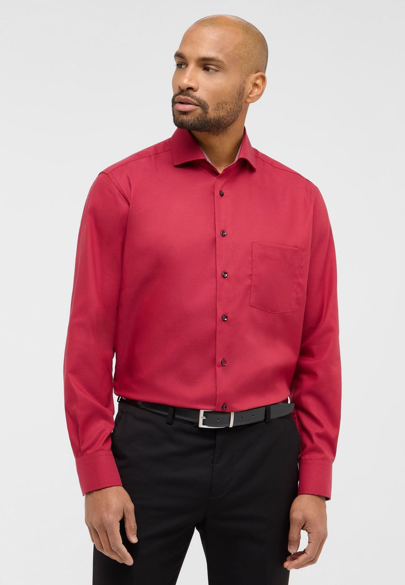 Rotes Longsleeve-Hemd aus glattem Stoff, mit einem Button-Down-Kragen, einer Brusttasche und schwarzen Knöpfen. Getragen mit schwarzen Hosen und einem Gürtel.