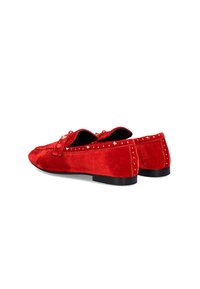 Mocasines de ante rojo con suelas negras planas, que presentan tachuelas doradas a lo largo de los bordes y un lazo decorativo en la parte frontal. Textura suave y diseño limpio.