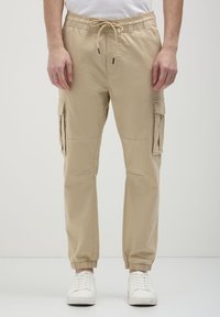 Pantaloni cargo beige con polsini e vita elasticizzati, dotati di tasche laterali e vestibilità comoda. Il materiale sembra leggero e liscio.