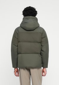 Groene pufferjack met capuchon, met een geborduurd ontwerp en een gladde textuur. De achterkant toont drie horizontale panelen en een relaxte pasvorm.