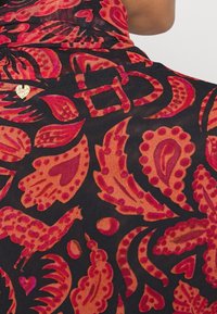 Tessuto nero trasparente con intricati motivi paisley in rosso e rosa, arricchito da un piccolo cuore dorato. Texture liscia, design fluido.