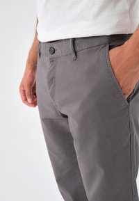 Šedé bavlněné kalhoty s předním zapínáním na knoflík, bočními kapsami a hladkým povrchem, vystihující přiléhavý střih a casual design.