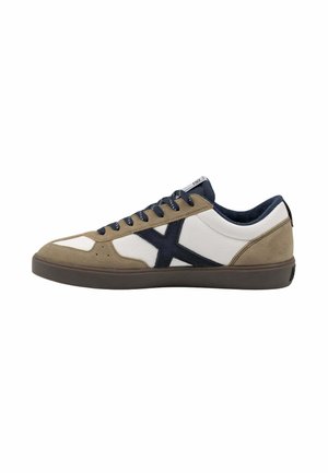 Zapatilla baja con paneles de ante blanco y beige, cordones azul marino y un diseño en X azul marino en el lateral con suela marrón oscuro.