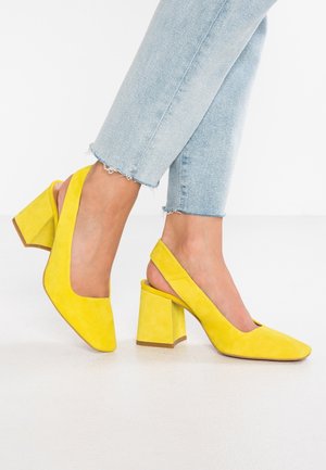 Jalat, joissa on kirkkaan keltaiset slingback-lohkopistokkaat, yhdistettynä vaaleansinisiin, rispaantuneilla helmoilla varustettuihin lyhennettyihin farkkuihin.