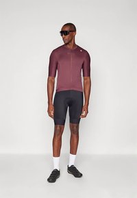 Biciklistički dres u boji burgundca, s kratkim rukavima i prednjim patentnim zatvaračem. Nošen s crnim jastučićima kratkim hlačama, bijelim čarapama i crnim biciklističkim cipelama.