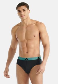 Czarne męskie slipy z turkusowym elastycznym pasem w talii, na którym znajdują się trzy czarne paski. Gładka tkanina, dopasowany krój oraz przeszycia z przodu.