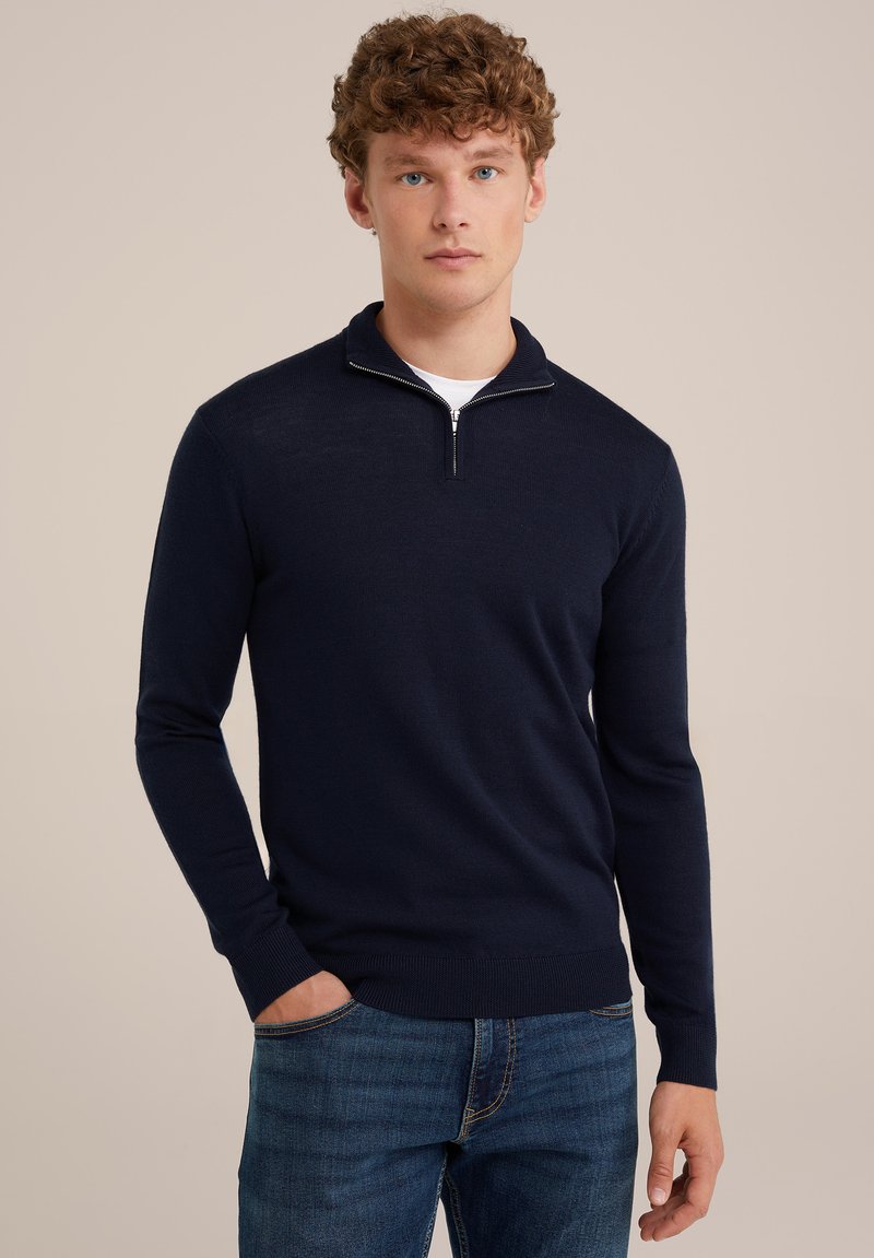 Jersey de punto azul marino con cuello de media cremallera, mangas largas y puños acanalados. Colocado sobre unos jeans de mezclilla, con una textura de tela suave.
