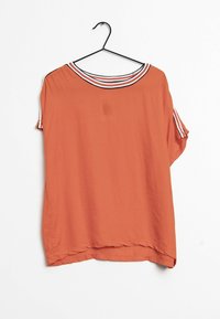 Blusa arancione a maniche corte, morbida, con colletto a righe bianche e nere e rifiniture sulle maniche, appesa a un gruccia nera su uno sfondo bianco.