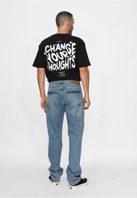 Svart t-skjorte med hvit grafisk tekst på ryggen, kombinert med lyseblå denimjeans med flere lommer og en avslappet passform.