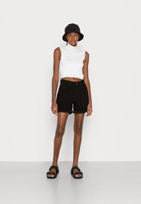 Μαύρα τζιν σορτς με διπλωμένα μανίκια, συνδυασμένα με λευκό ριμπ μίνι τοπ και μαύρο καπέλο τύπου bucket. Οι μαύρες σαγιονάρες ολοκληρώνουν το σύνολο.