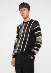 Strikket sweater med et geometrisk mønster i sort, brun og hvid; rund halsudskæring; ribbede manchetter og kant.