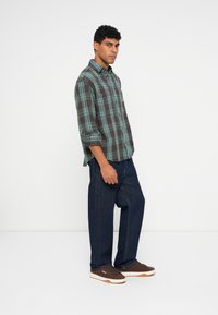 Rutet flannel skjorte i mørkebrun og teal, med opsmøgede ærmer. Sat sammen med mørkeblå denim jeans og brune sneakers.