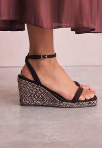 Sandale maro din piele intoarsa cu platforma, cu toc împletit din iută și o curea la gleznă cu cataramă auriu. Design neted la vârf și călcâi.