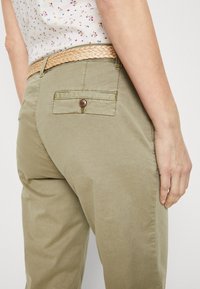 Zelenohnědé kalhoty z bavlněné směsi s pleteným béžovým páskem, zadní kapsy s knoflíkovým zapínáním a hladkou texturou.