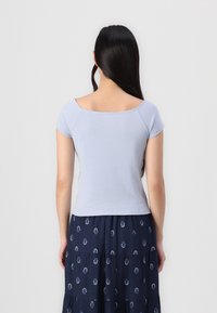 Top justo azul claro com mangas curtas, decote largo e textura canelada, emparelhado com uma saia navy estampada com pequenos detalhes brancos.
