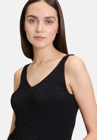 Débardeur noir à côtes avec un décolleté en V. Présente des accents scintillants subtils et des bretelles larges. Tissu doux, coupe ajustée.