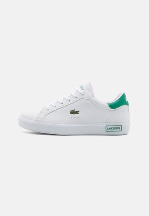 Sapatilhas brancas de atacadores com um detalhe verde no calcanhar, apresentando um pequeno logótipo de crocodilo bordado e mínimas perfurações em forma de ponto na lateral.