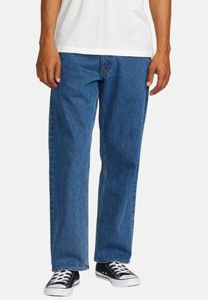 Blue denim jeans with a straight cut, five-pocket design, and contrasting stitching, paired with black low-top sneakers.