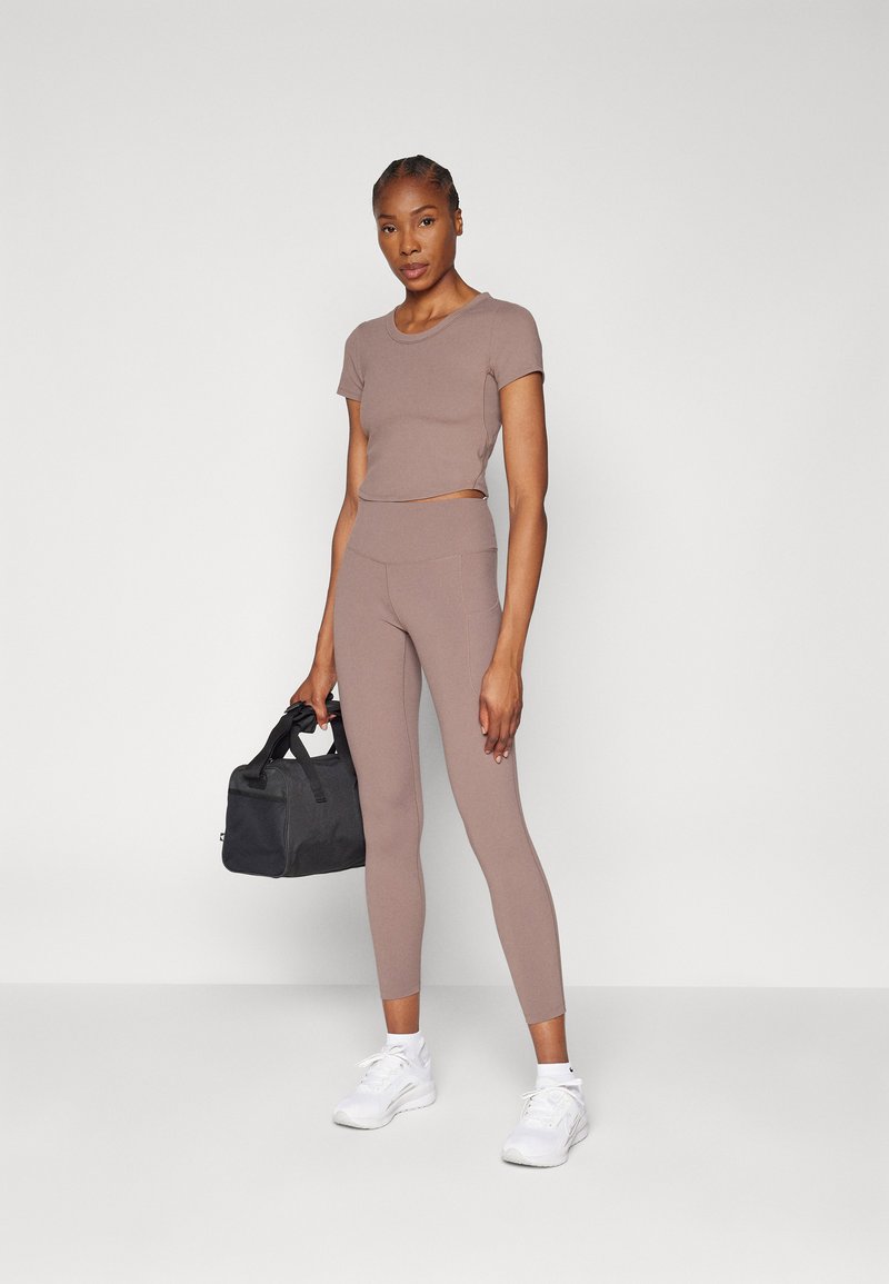 Ensemble de vêtements de sport marron clair composé d'un haut court à manches courtes et de leggings taille haute. Comprend un sac de sport noir et des chaussures de sport blanches.