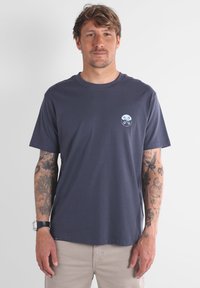 T-shirt bleu marine à manches courtes en coton avec un col rond et un petit graphique circulaire bleu sur la poitrine. Surface texturée.