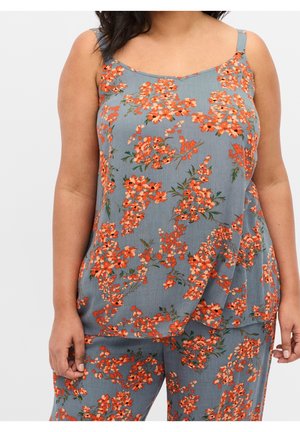 Femme portant un haut sans manches bleu-gris et un pantalon assorti avec un motif floral orange, debout les bras détendus le long du corps.