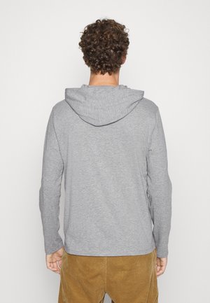 Sudadera gris de manga larga con capucha ajustable, con textura suave y un corte relajado, combinada con pantalones de pana color canela.