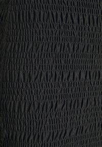 Mustaa kangasta, jossa on tiheästi rypytetty smokkikuvio, mikä luo tekstuurin ja rypistyneen ulkonäön pinnalle.