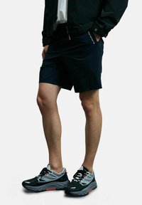 Shorts de sport bleu foncé au design épuré avec une poche latérale, associés à des chaussures de course noires et grises avec des accents rouges.