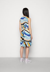 Pestrobarevné šaty bez rukávů s vlnitým vzorem a vypasovaným pasem; nošeny s levandulovými sneakers s vysokým střihem. Hladká látka, délka po kolena.