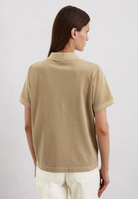 Beige polo shirt met korte mouwen, voorzien van een kraag en een soepele textuur. Het shirt heeft een ontspannen pasvorm en reikt tot de taille.