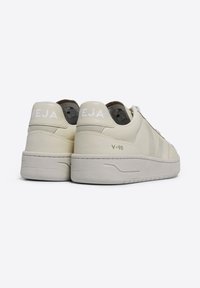 Ljusbeiga sneakers med överdel i slät läder, vita detaljer och vadderad krage. Har en texturerad sula och "VEJA V-90"-logotyp på hälen.