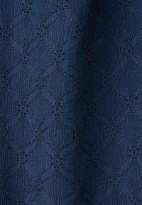 Tessuto blu navy con motivo a diamante strutturato e piccoli fori che formano forme floreali all'interno del disegno.