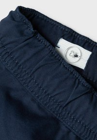 Tissu en coton bleu marine avec une surface texturée, présentant une étiquette blanche et un bouton transparent au col, mettant en valeur les détails de couture.