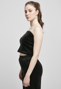 Haut cropped en velours noir à une épaule avec une texture lisse, associé à un pantalon en velours noir taille haute, featuring une ceinture élastique.