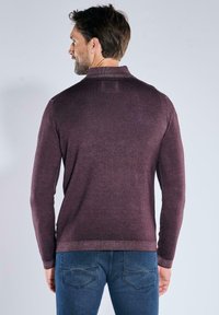 Dunkelviolettes, strukturiertes Pullover-Sweatshirt mit ribbeltem Kragen und langen Ärmeln, kombiniert mit blauen Jeans. Sichtbare Nähte.