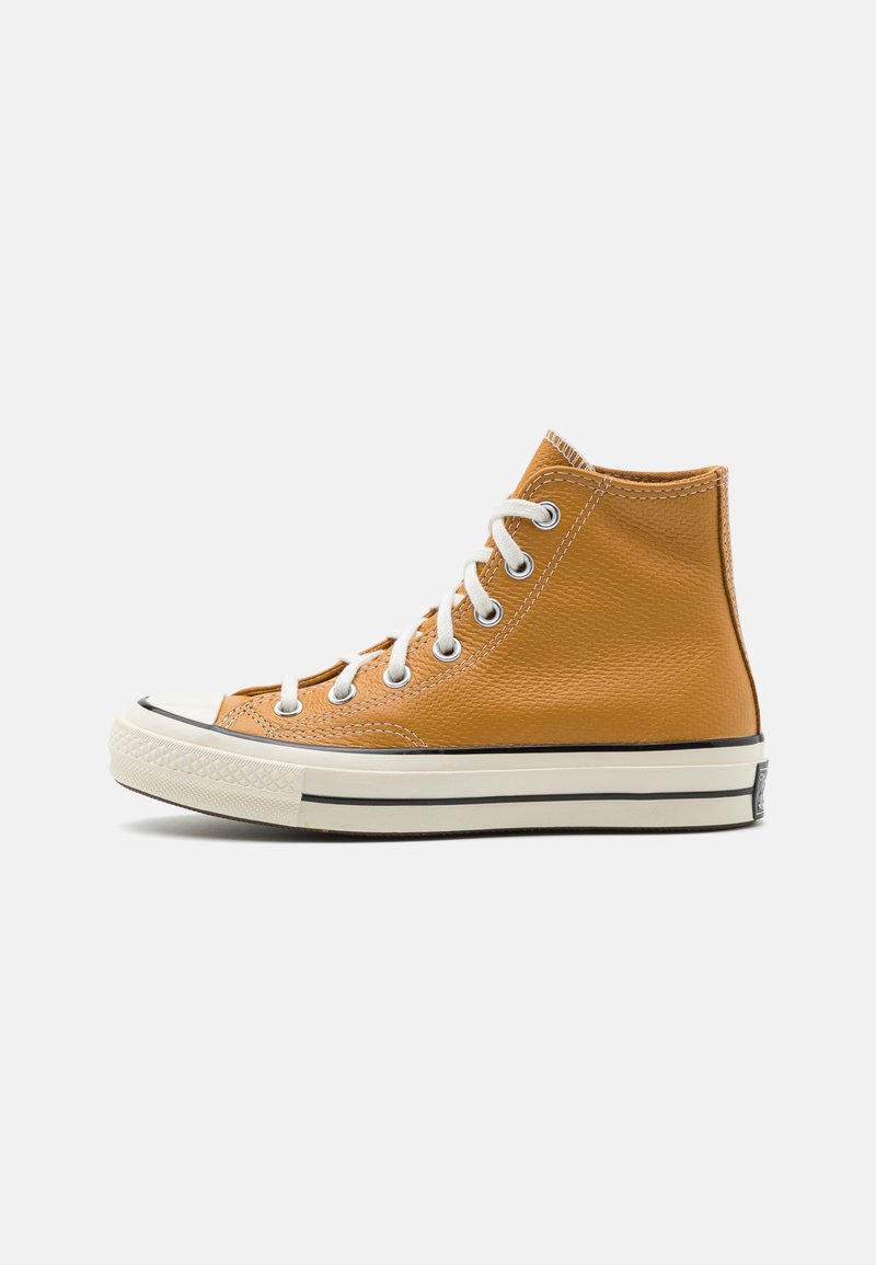 Høye sneakers i teksturert oransje lær, hvite snører og gummitåhette, med en svart stripe langs sålen.