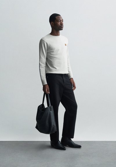 Maglione grigio a maniche lunghe con un piccolo logo, pantaloni neri e una borsa a tracolla in pelle nera. Texture liscia, design semplice, silhouette aderente.