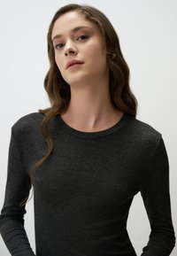 Langärmliges, dunkelgraues Oberteil aus weichem, strukturiertem Stoff mit Rundhalsausschnitt und tailliertem Design. Einfacher, minimalistischer Stil.