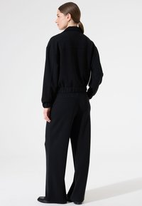 Schwarzes Sportset mit einer lässigen, cropped Jacke mit elastischem Bund und passenden weit geschnittenen Hosen. Weicher Stoff mit minimalen Nähten.