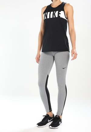 Canotta nera senza maniche Nike con grande logo bianco; leggings grigi con pannelli laterali neri; scarpe da ginnastica nere.