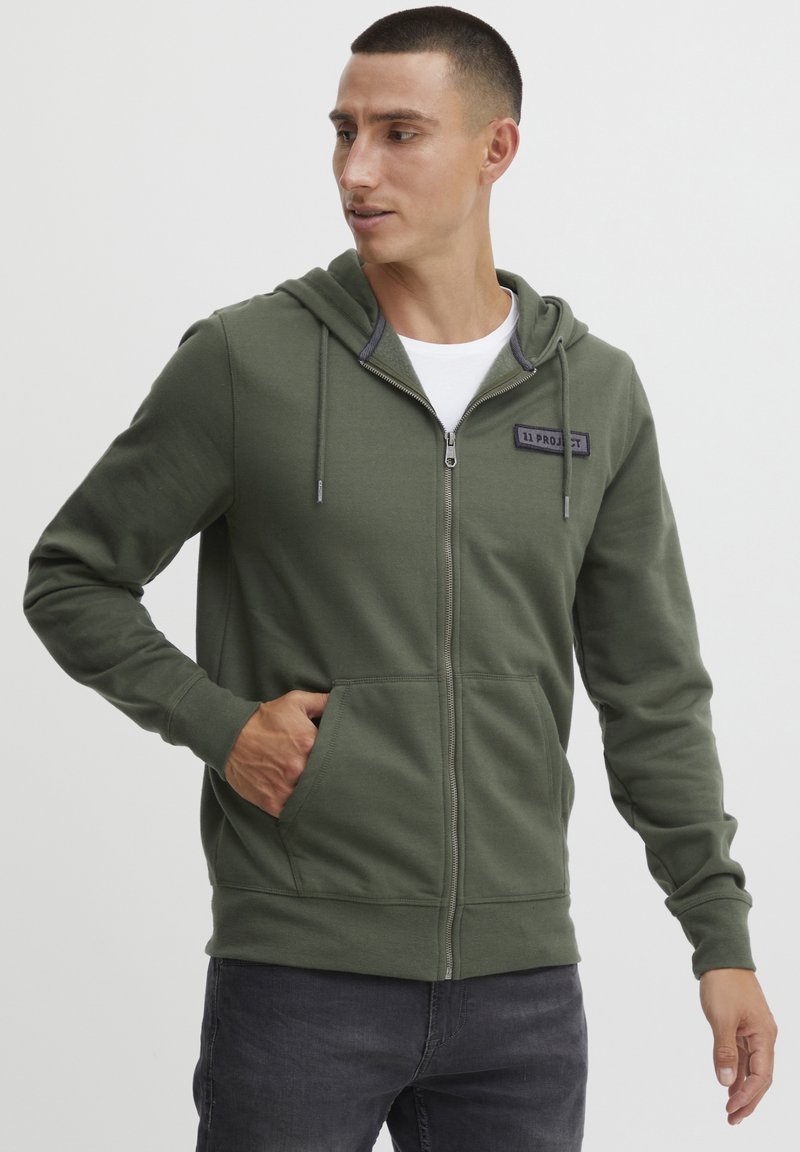 Grøn zip-up hoodie lavet af bomuldsblanding, med en kengurupocket, snøre-hætte og en lille brand-patch på brystet.