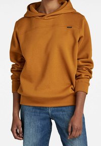 Sudadera amarilla mostaza hecha de una suave mezcla de algodón, con un corte holgado, capucha ajustable con cordón y un logotipo sutil en el pecho.