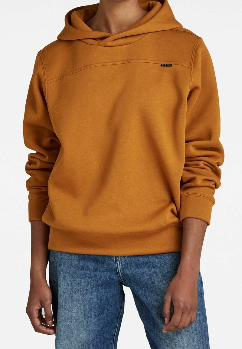 Sudadera amarilla mostaza hecha de una suave mezcla de algodón, con un corte holgado, capucha ajustable con cordón y un logotipo sutil en el pecho.