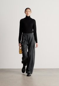 Camisola de gola alta preta, calças largas cinza e uma pequena mala amarela; modelo a usar sapatos pretos; fundo simples.