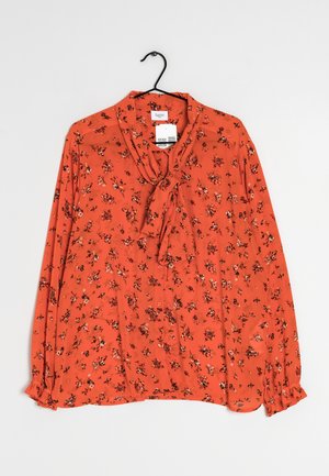 Oranje blouse met lange mouwen met kleine bloemenprint, strikjescollar, knopen aan de voorkant en elastische gerimpelde manchetten aan een zwarte hanger.